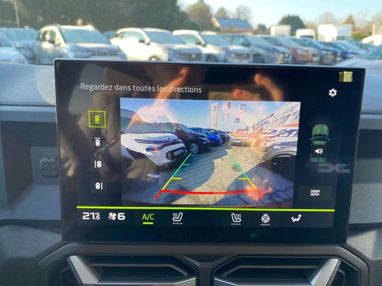 Écran de caméra de recul du Dacia Duster 2024 montrant un parking ensoleillé avec plusieurs véhicules visibles.