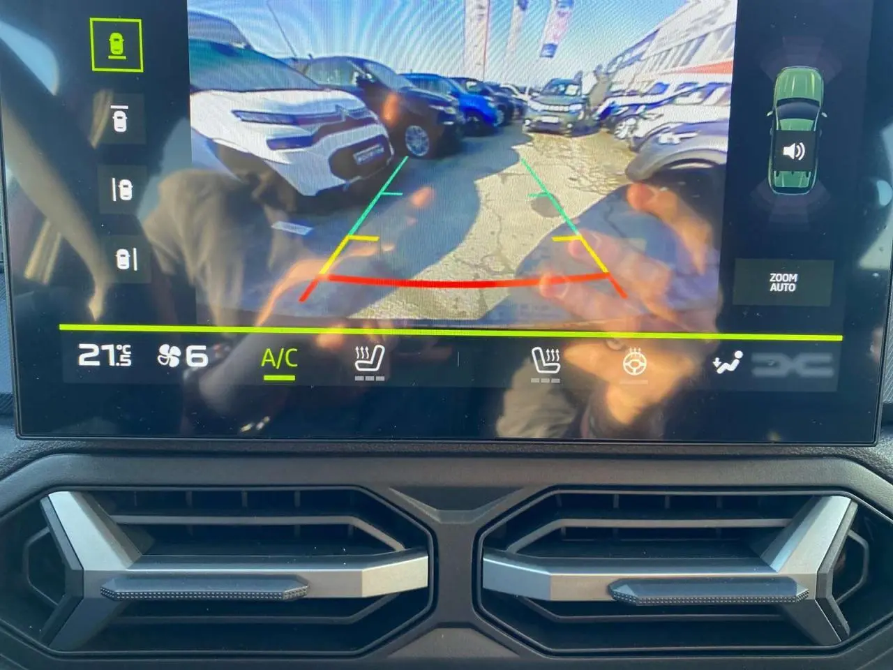 Vue écran caméra de recul du Dacia Duster 2024 brun terracotta montrant un parking avec plusieurs véhicules.