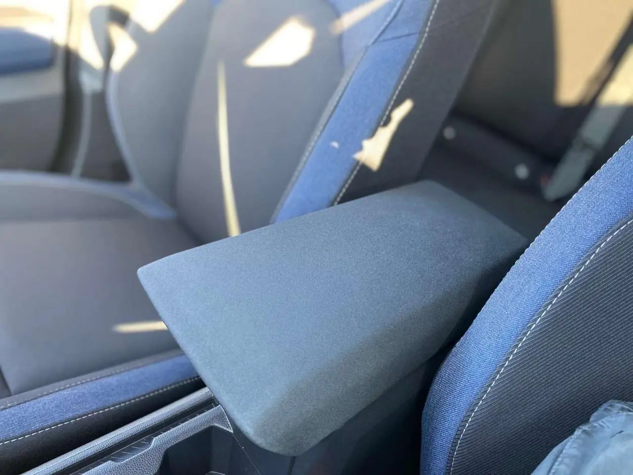 Accoudoir central en tissu gris entre les sièges avant bleu foncé du Dacia Duster 2024.