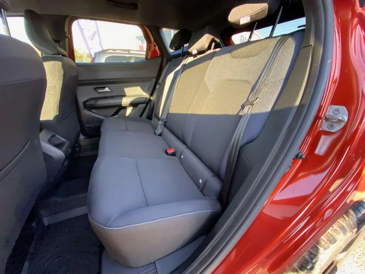 Vue côté droit des sièges arrière noirs du Dacia Duster 2024 brun terracotta avec porte ouverte au soleil.