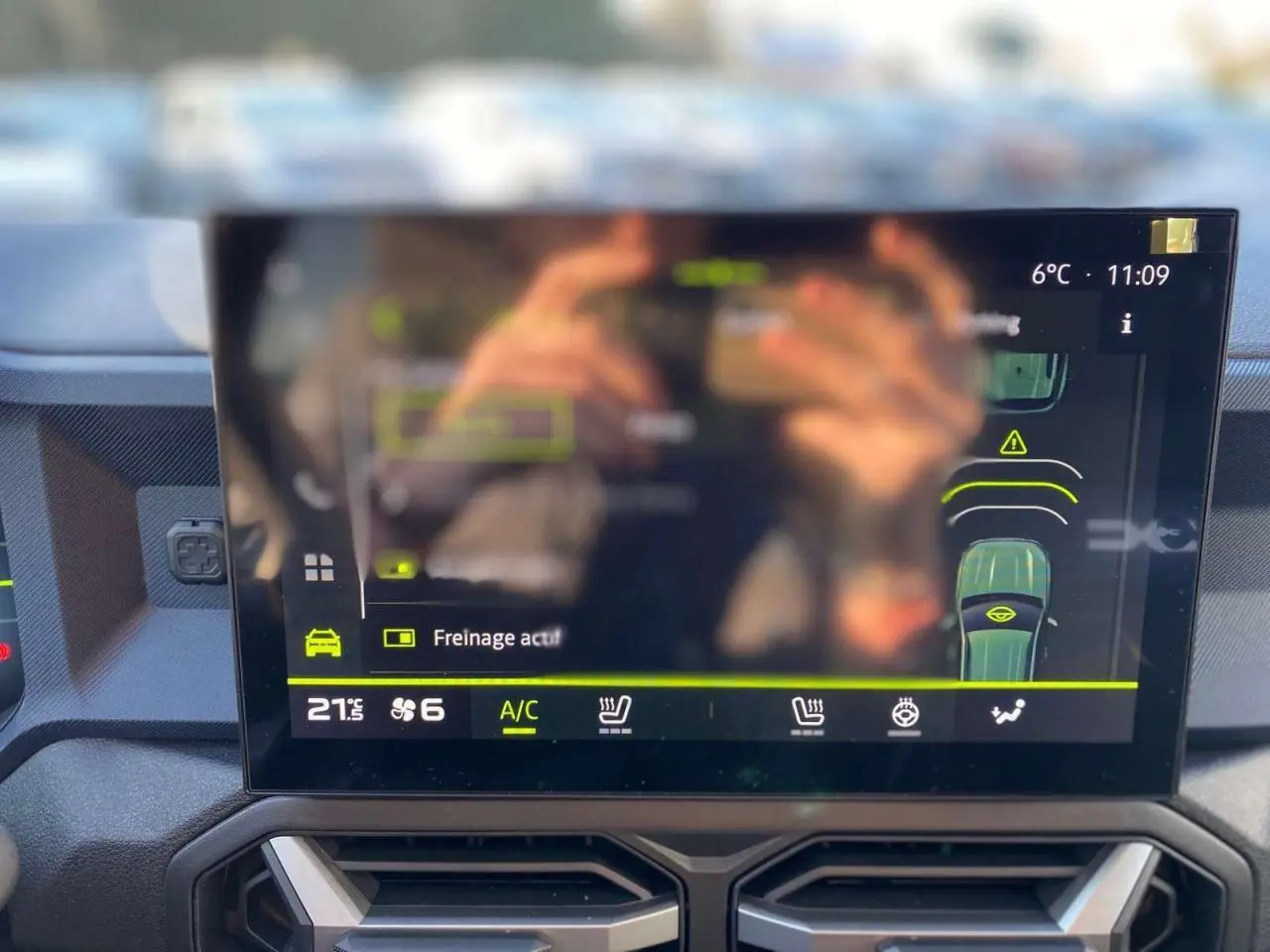 Écran tactile central du Dacia Duster 2024 affichant l'aide au freinage et la climatisation, vue intérieure frontale.