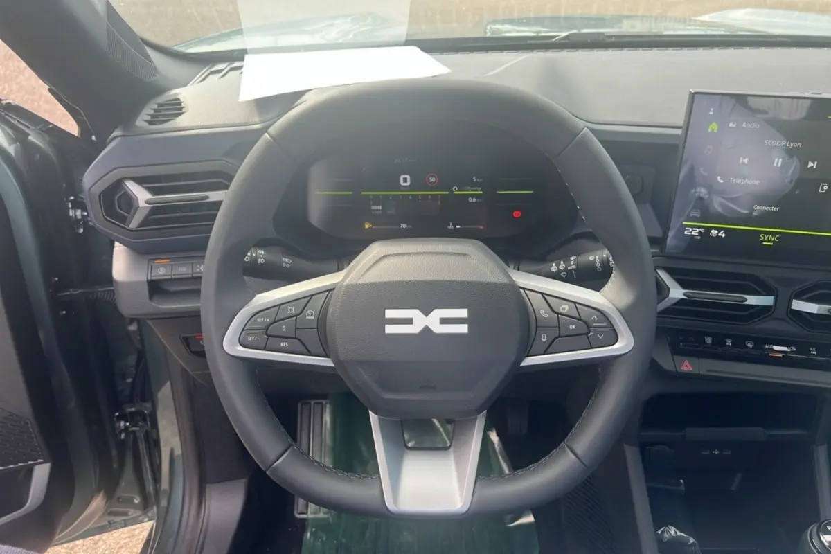 Vue intérieure centrée sur le volant multifonction du Dacia Bigster 2025 avec tableau de bord digital et écran tactile.