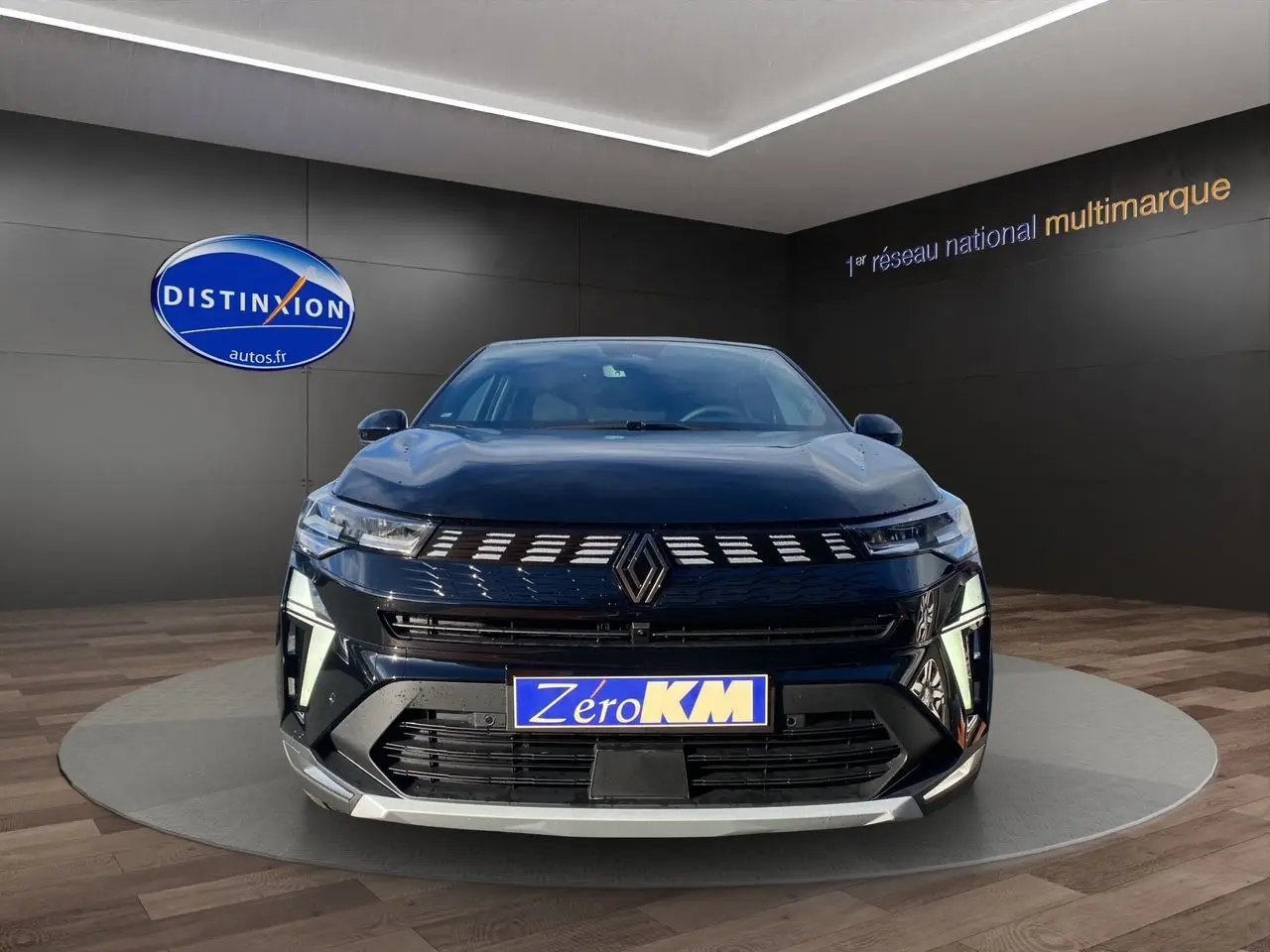 Vue de face d'une Renault Symbioz noire étoile avec calandre lumineuse et plaque Zéro KM dans un showroom.