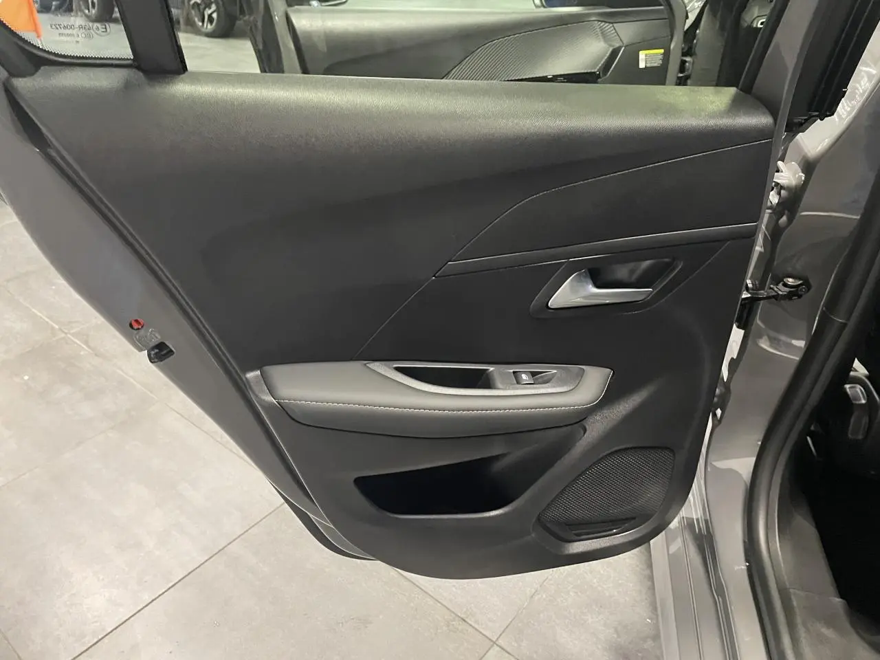 Porte arrière gauche ouverte d'une Peugeot 208 gris selenium, montrant la garniture noire avec accoudoir et haut-parleur intégré.