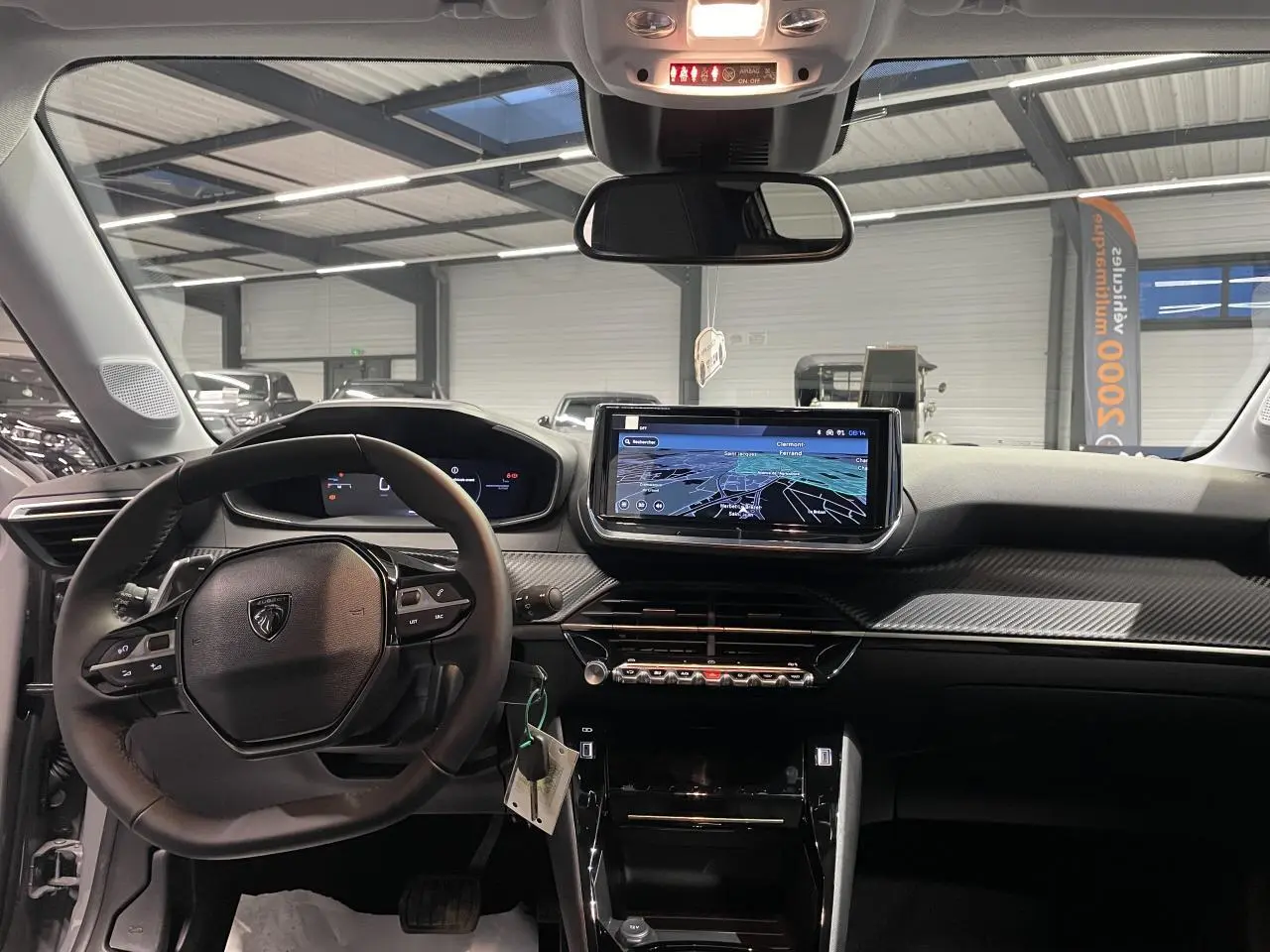 Vue intérieure avant du tableau de bord de la Peugeot 208 2025 avec écran tactile et volant compact noir.