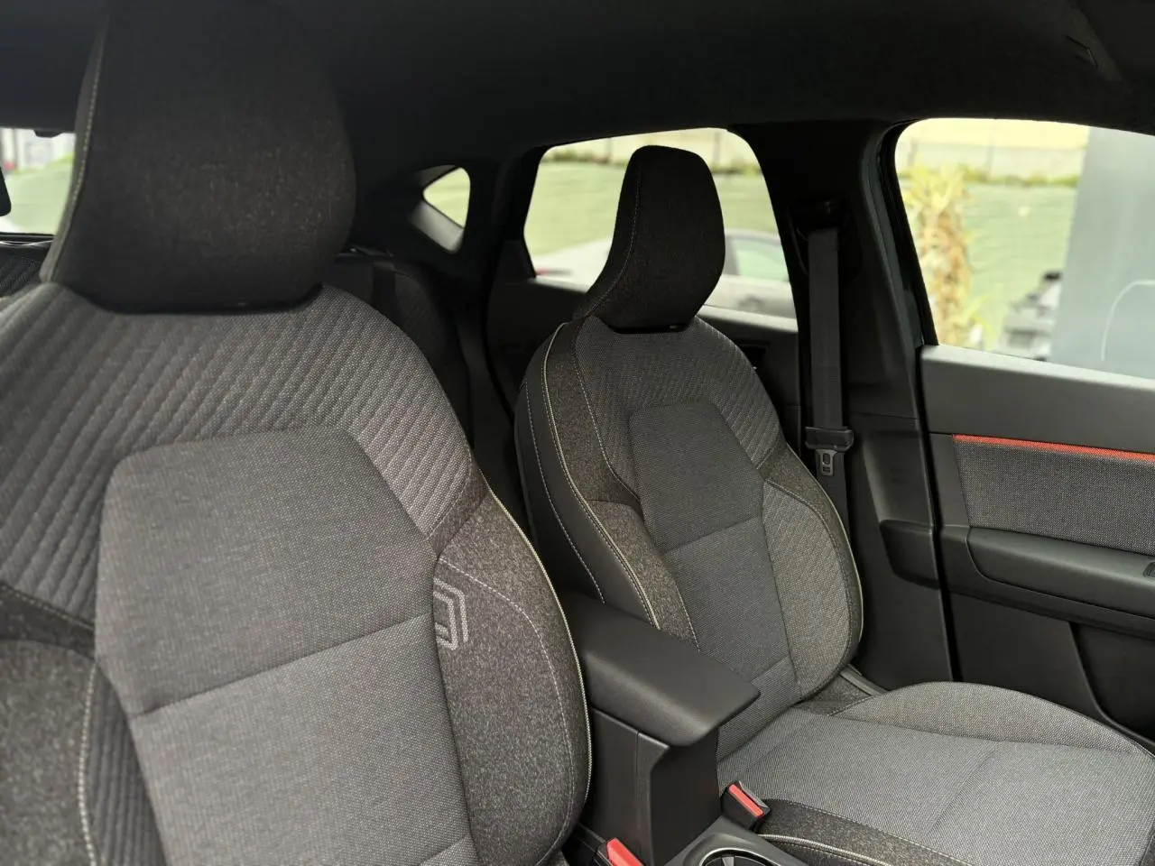 Vue intérieure des sièges avant gris avec coutures contrastantes et accoudoir central du Renault Captur 2025 noir étoile.