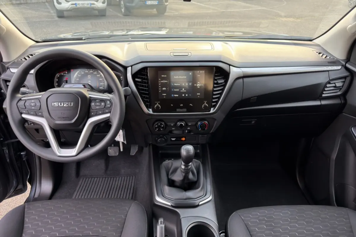 Vue intérieure avant de l'Isuzu D-MAX 2.2 TD 164 Space Evolution, tableau de bord et volant multifonctions noirs.