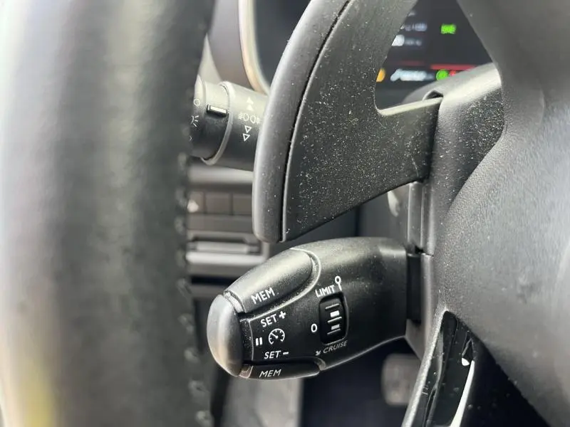Gros plan sur la commande de régulateur de vitesse noire derrière le volant d'un Citroën C5 Aircross blanc.