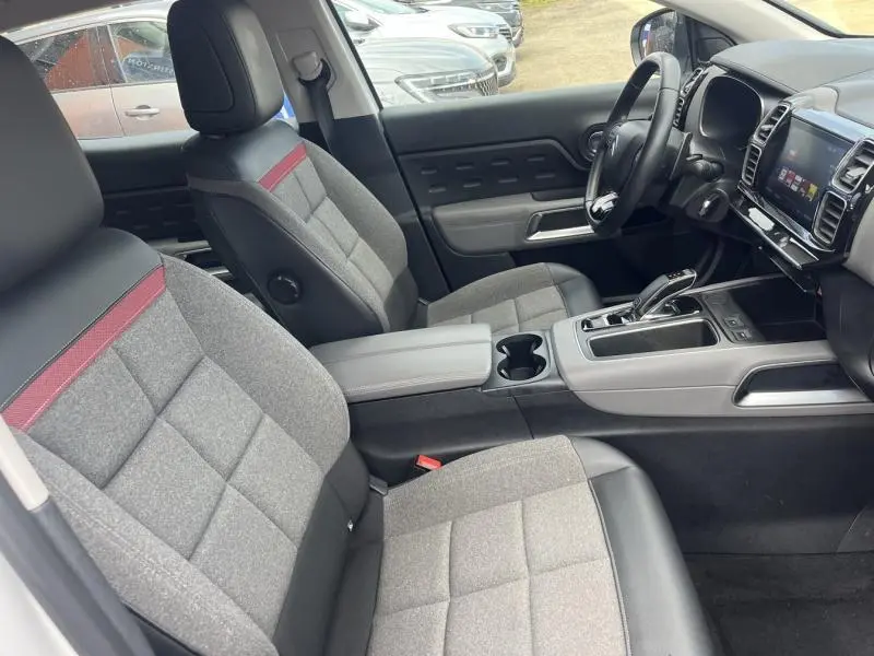 Intérieur avant du Citroën C5 Aircross blanc, sièges tissu gris avec bande rouge, console centrale et volant multifonction visibles.