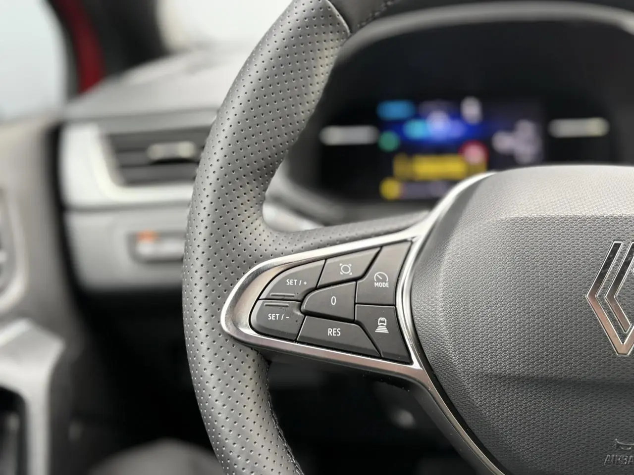 Gros plan sur le volant perforé gris du Renault Captur 2025 avec commandes intégrées et tableau de bord numérique flou.