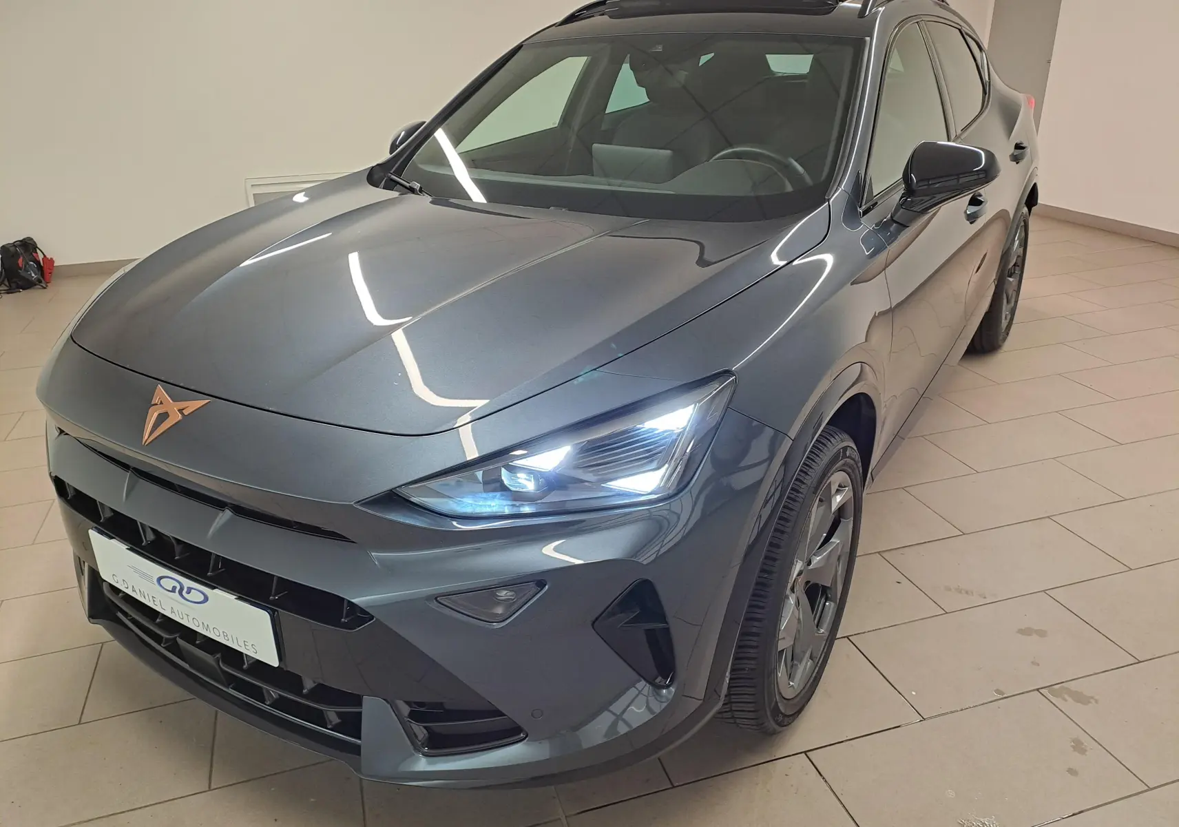 Vue 3/4 avant droit du CUPRA Formentor gris magnétique avec toit ouvrant et feux LED allumés en intérieur showroom.