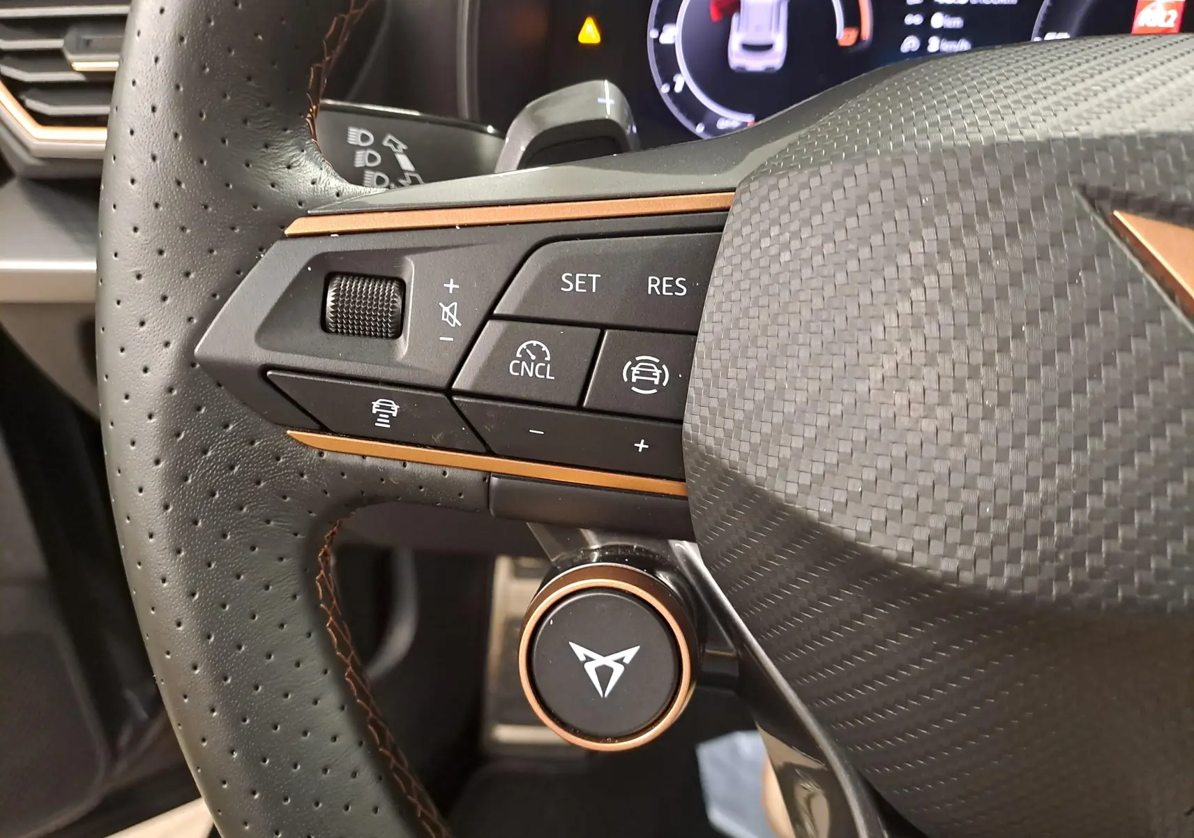 Gros plan sur le volant cuir perforé noir du CUPRA Formentor avec boutons de commande et logo cuivré au centre.