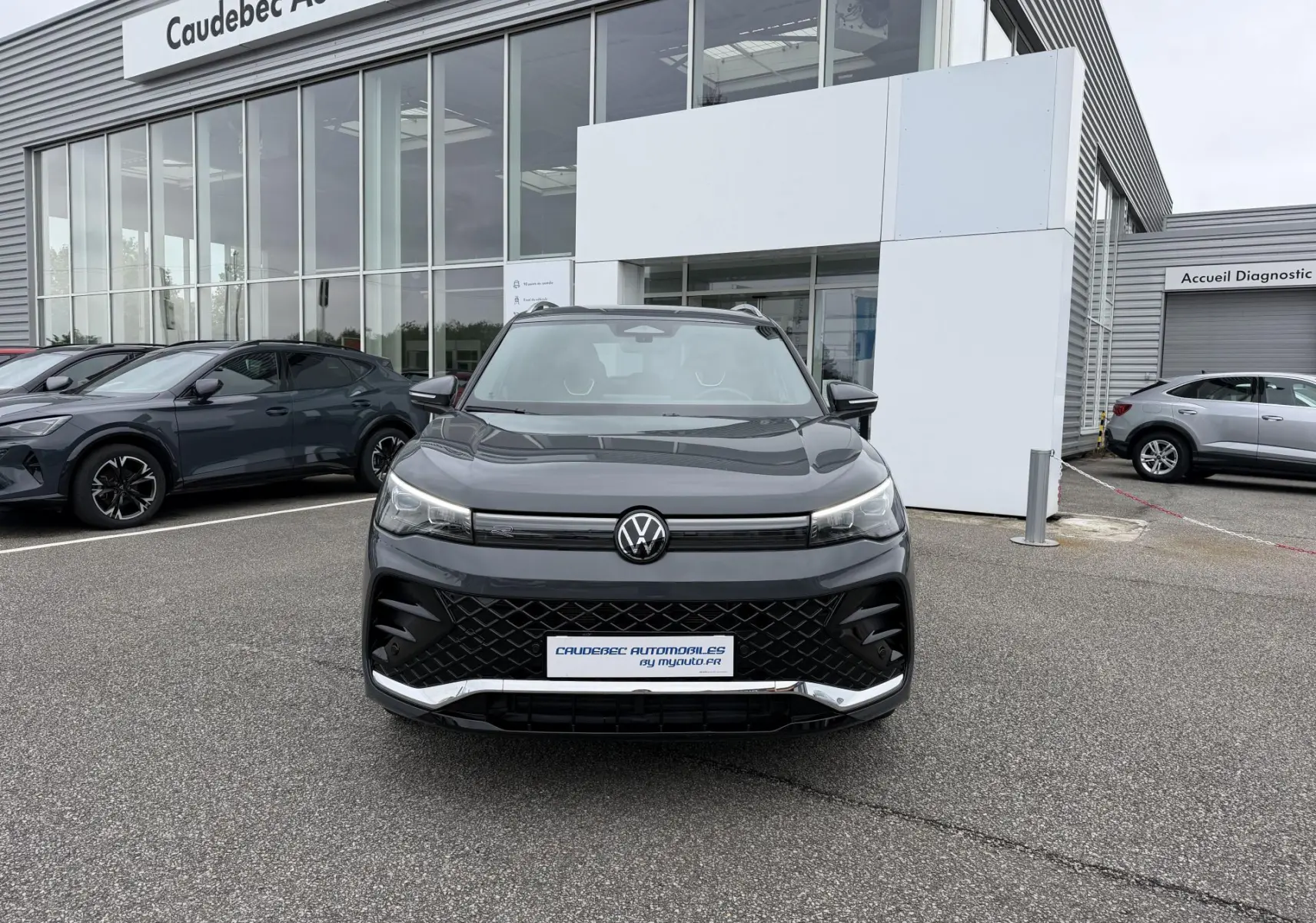 Volkswagen Tiguan gris métallisé vu de face, avec calandre noire et projecteurs LED allumés, devant un showroom.