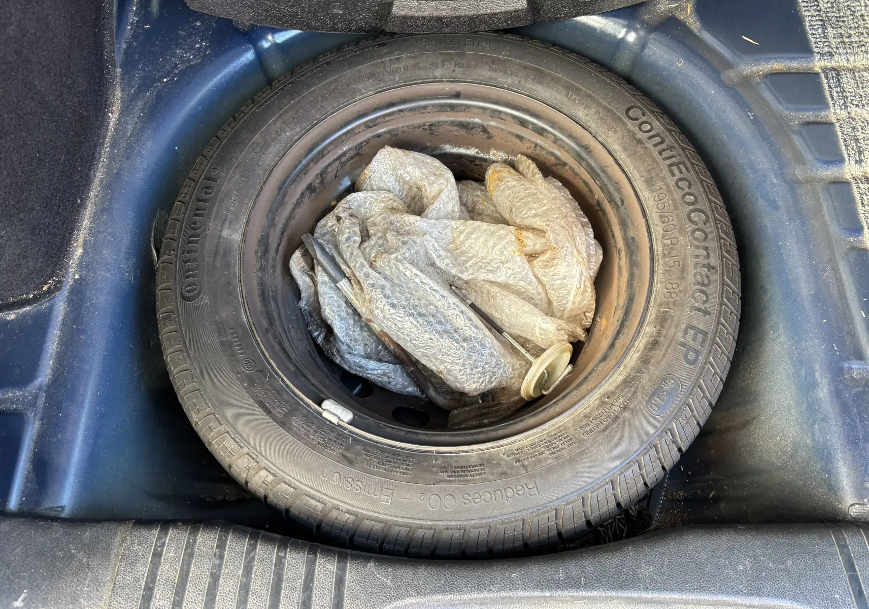 Vue plongeante sur la roue de secours dans le coffre bleu d'une Ford Fusion 2009, pneu Continental avec outil emballé.