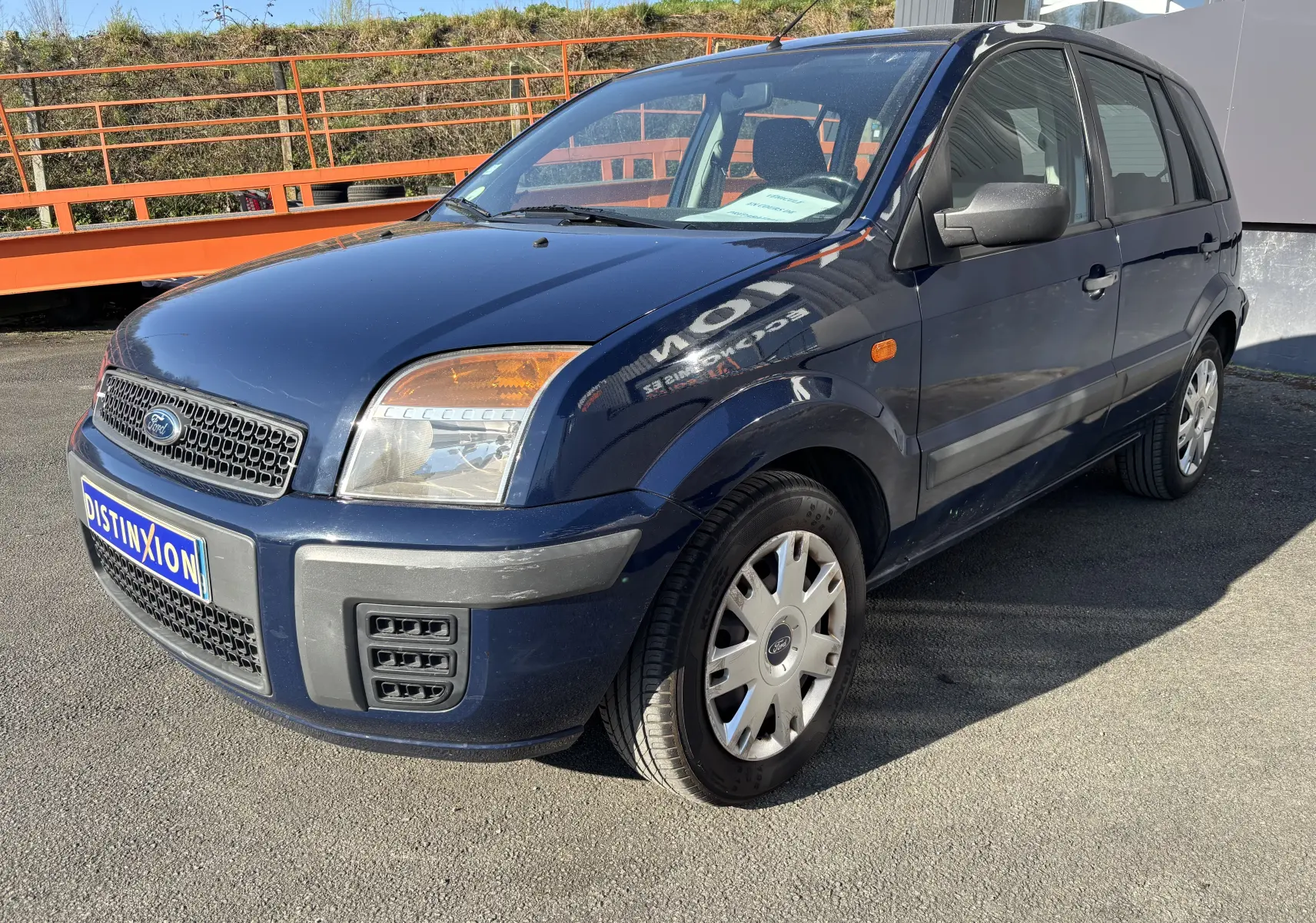 Ford Fusion bleu vue 3/4 avant droit, compacte cinq portes avec pare-chocs noir et jantes acier.