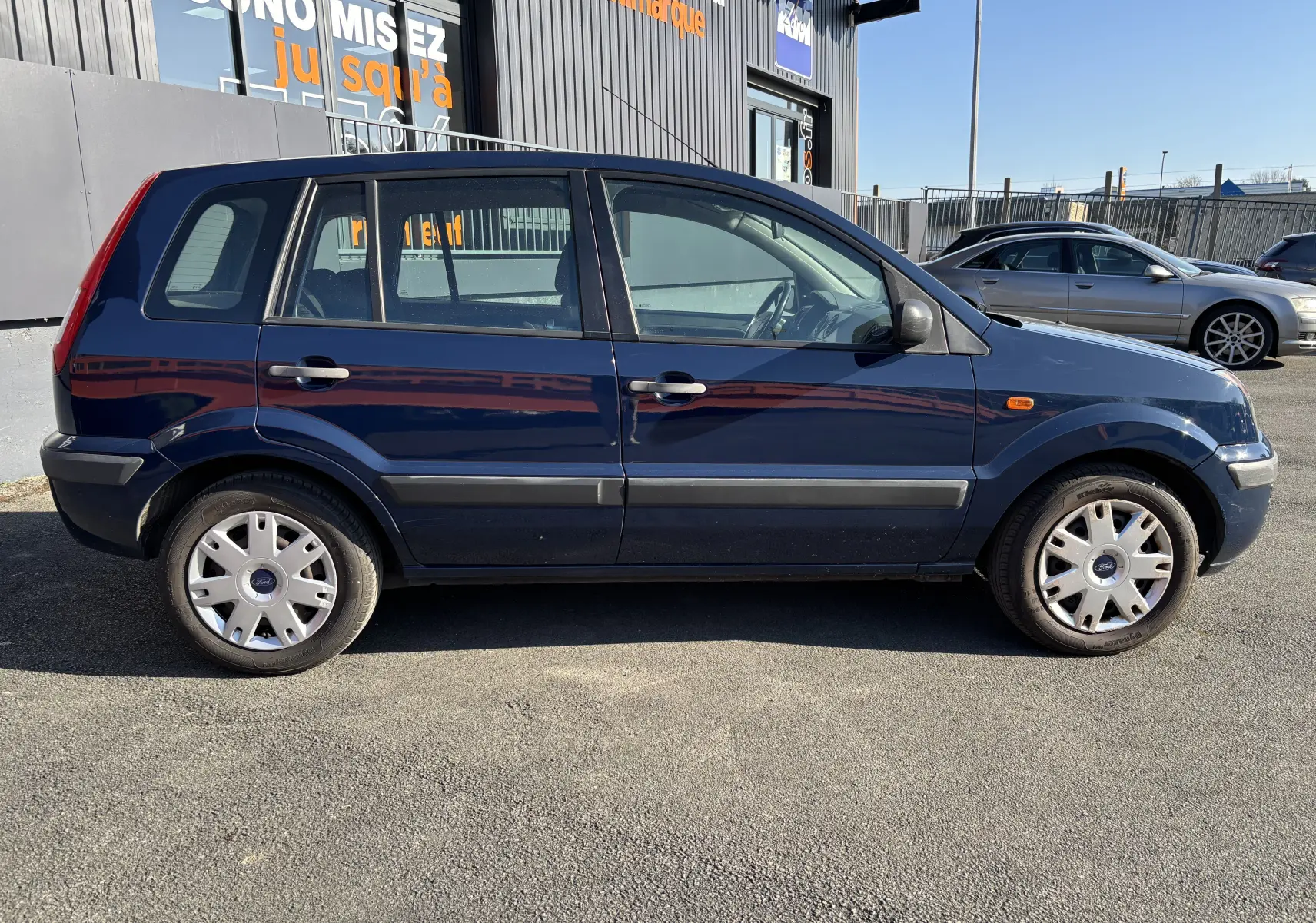 Ford Fusion bleu vue de profil côté gauche, compacte 5 portes avec jantes acier et enjoliveurs d'origine.