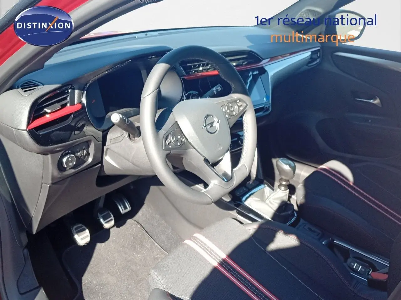 Vue intérieure de l'Opel Corsa 1.2 Turbo 2023 montrant le volant, la boîte manuelle et les sièges noirs avec surpiqûres rouges.