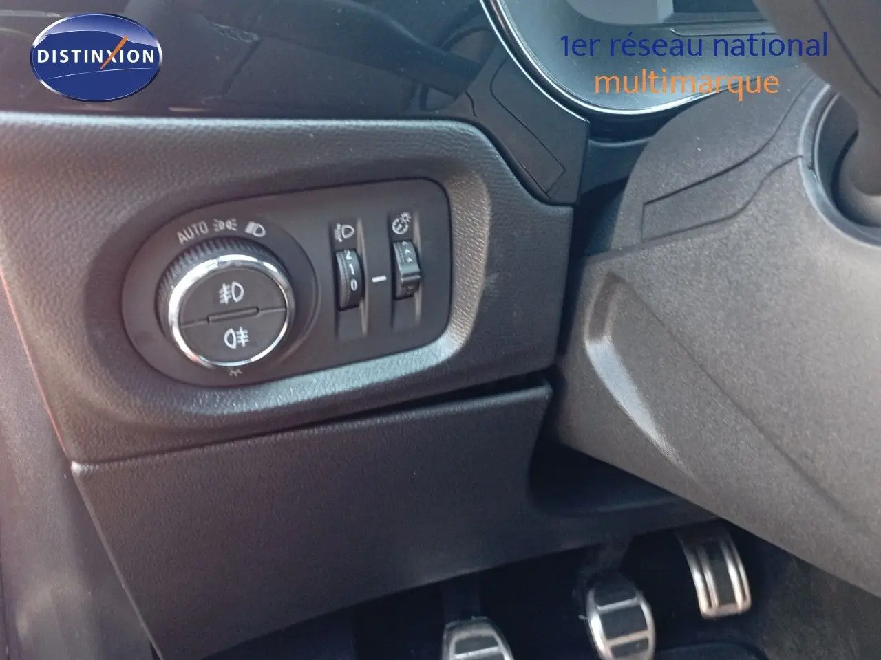 Gros plan sur les commandes d'éclairage et les pédales côté conducteur de l'Opel Corsa rouge métal 2023.