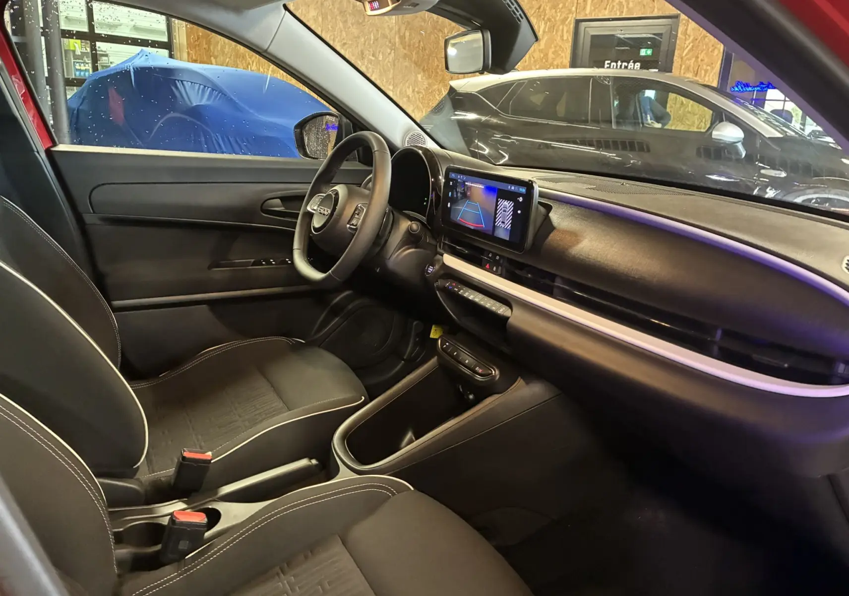 Vue intérieure côté conducteur de la FIAT 600 rouge 2024, avec tableau de bord noir et écran tactile affichant la caméra de recul.