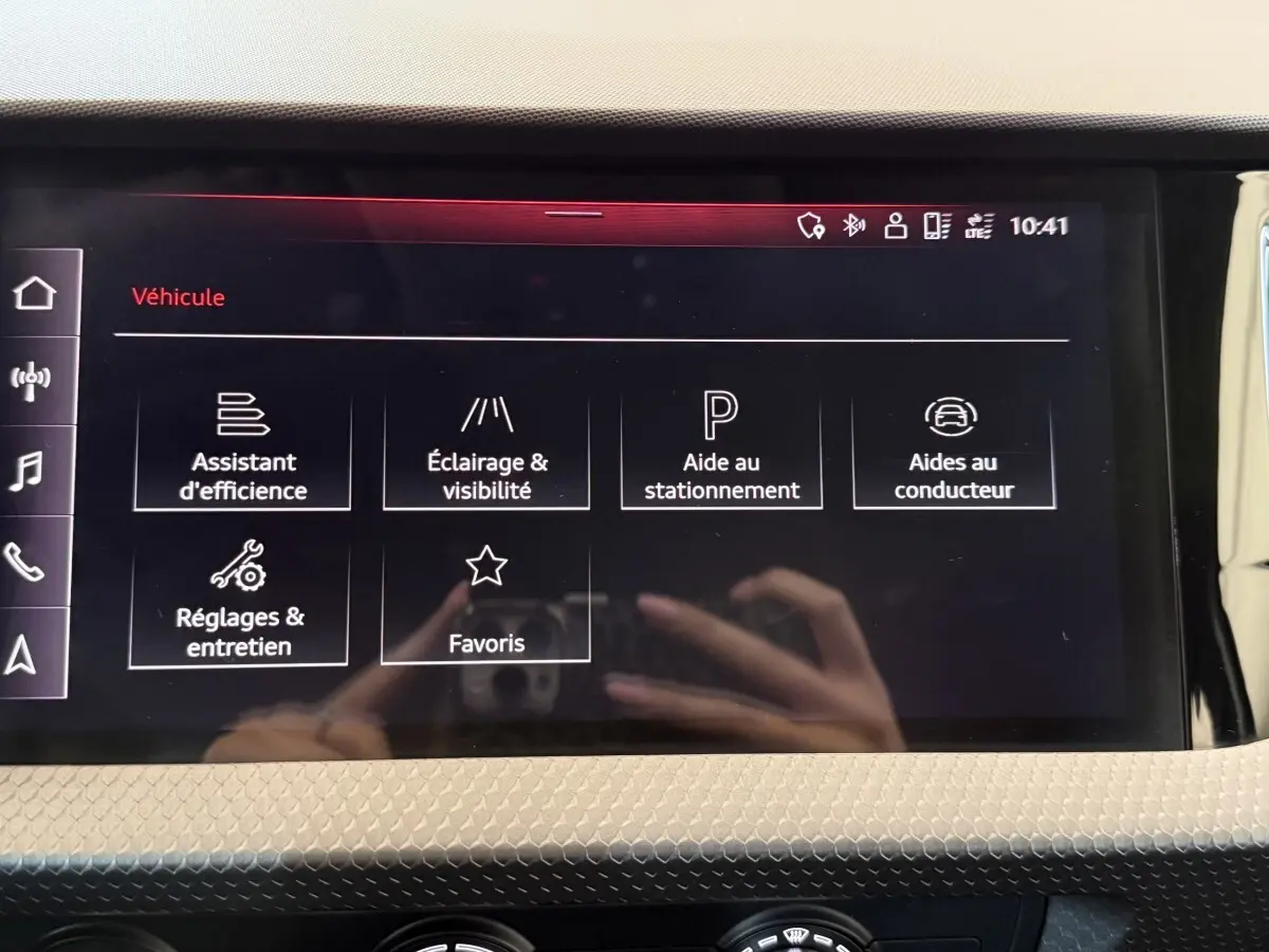Écran tactile central de l'Audi A1 noir, affichant les menus d'assistance et réglages du véhicule.