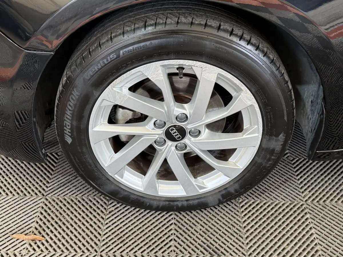 Gros plan sur la roue avant droite d’une Audi A1 noire, avec jante argentée et logo Audi au centre.