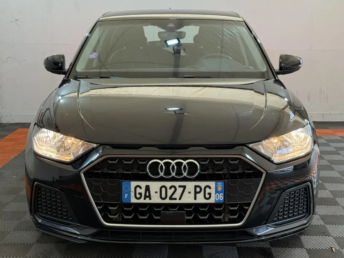 Vue frontale d'une Audi A1 noire 2021 avec calandre hexagonale et phares allumés dans un garage.