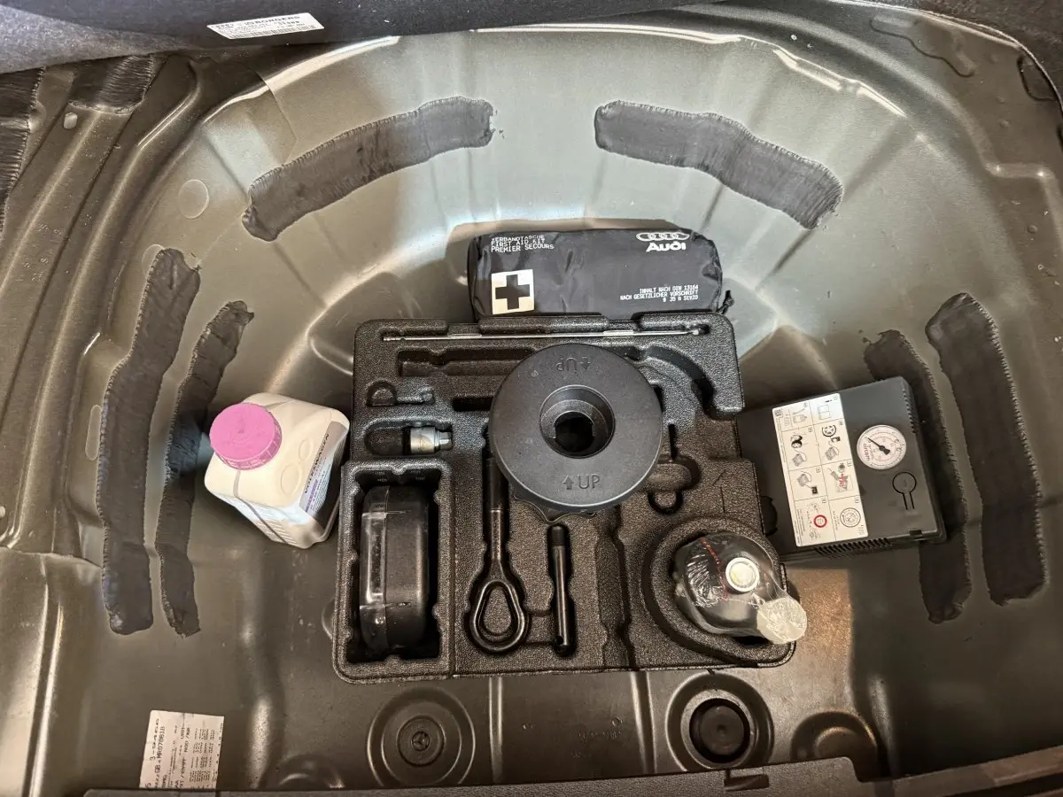 Vue plongeante sur le coffre noir d’une Audi A1 2021, montrant le rangement pour roue de secours et accessoires.