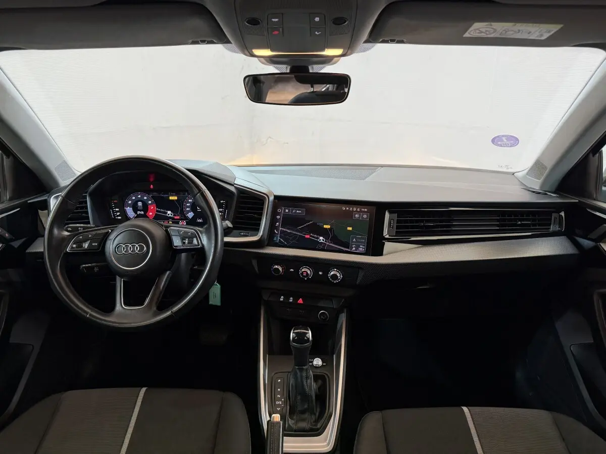 Vue intérieure avant de l'Audi A1 2021 noire, avec volant cuir multifonctions et écran tactile central affichant la navigation.