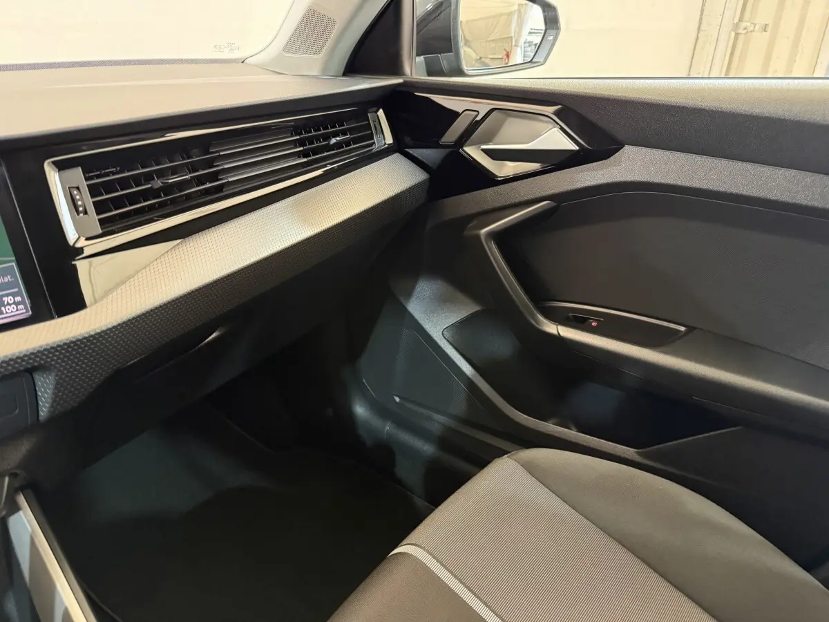 Vue intérieure côté passager de l'Audi A1 2021 noir, mettant en valeur la planche de bord et la portière moderne.