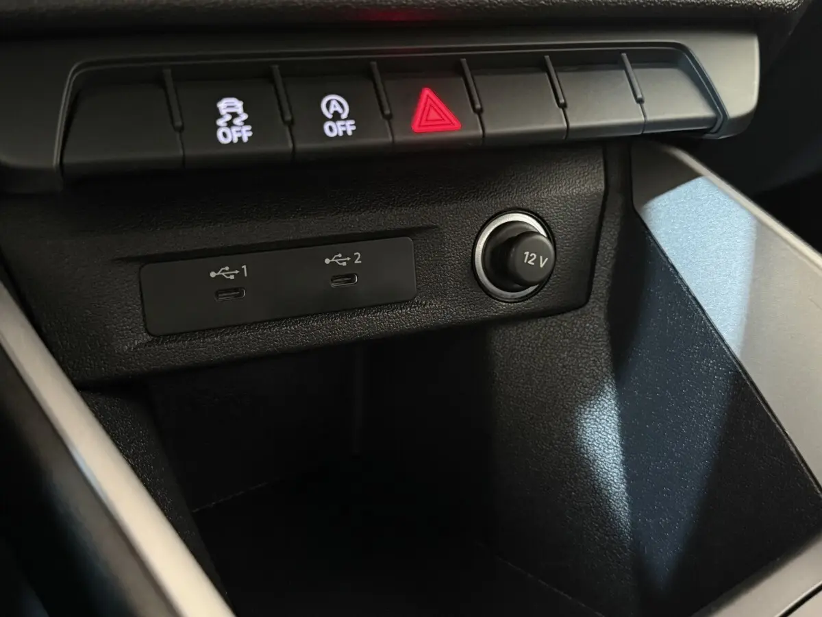 Vue rapprochée de la console centrale noire de l’Audi A1 2021, montrant prises USB et prise 12V avec boutons de contrôle.
