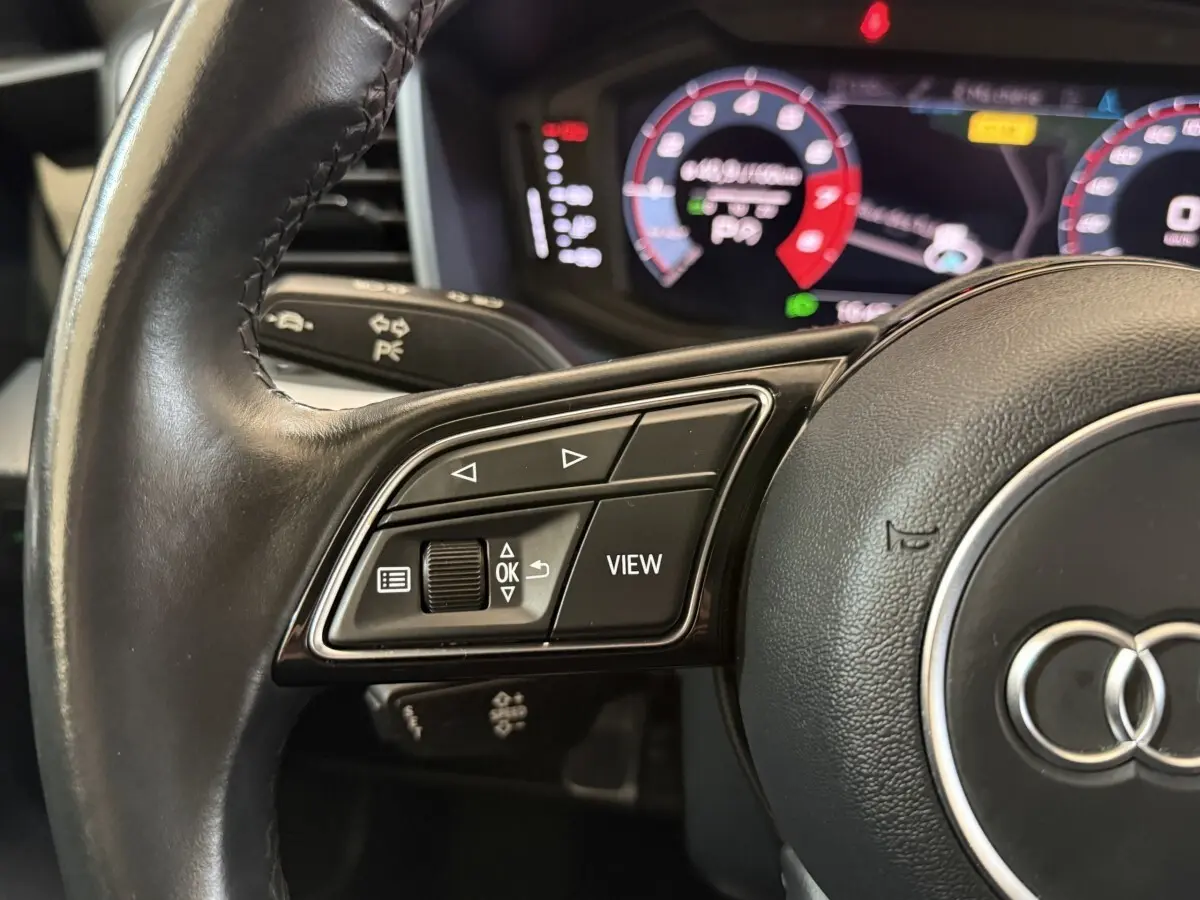 Gros plan sur le volant cuir noir multifonctions d'un Audi A1 2021 avec affichage numérique en arrière-plan.