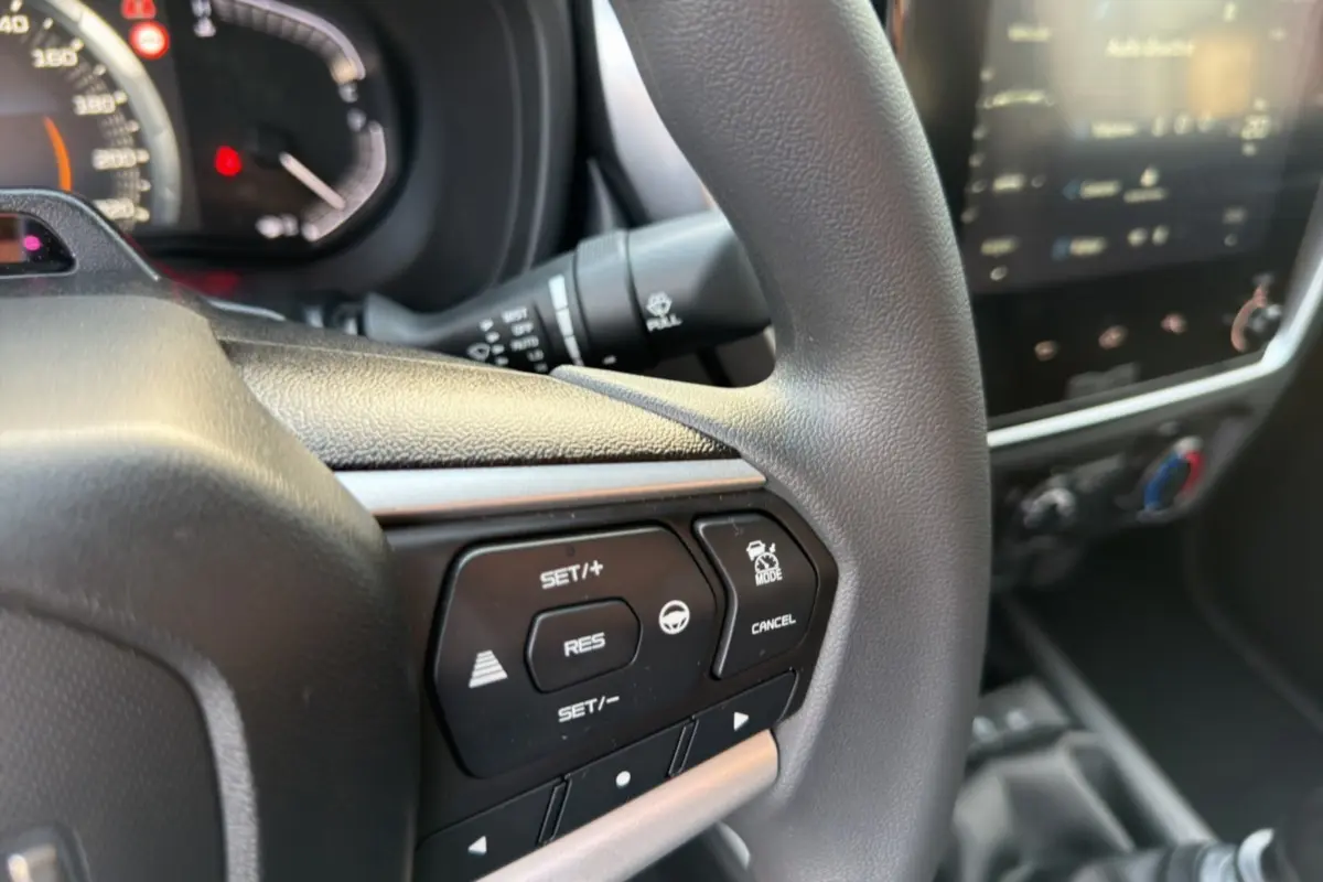 Gros plan sur le volant multifonctions de l'Isuzu D-MAX 2026 avec commandes de régulateur et écran tactile flou en arrière-plan.