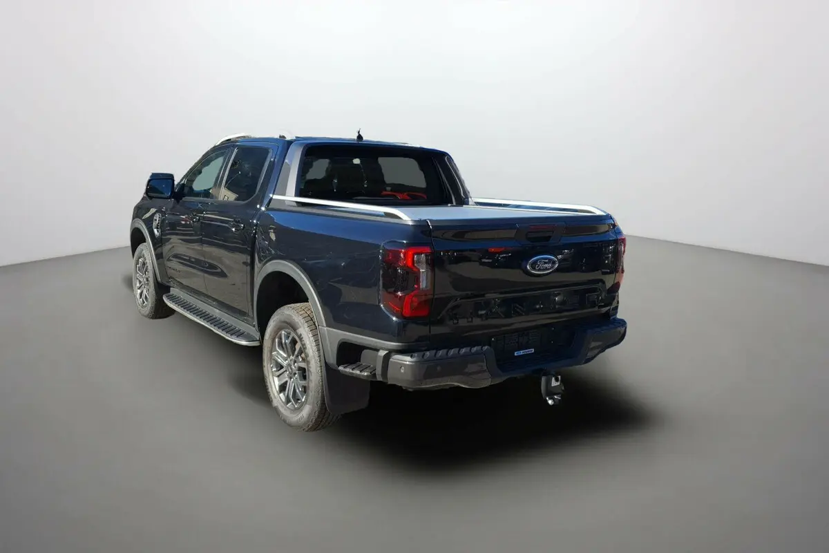 Ford Ranger Wildtrak noir agate vu en 3/4 arrière droit, avec ridelle et attelage visibles sur fond neutre.