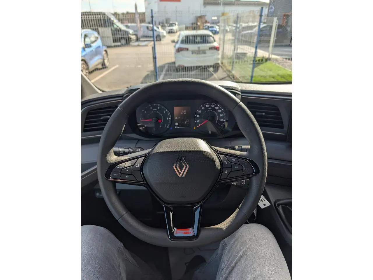 Volant noir avec logo Renault au centre, tableau de bord digital et compteur analogique, vue depuis le siège conducteur du Renault Master 2025.