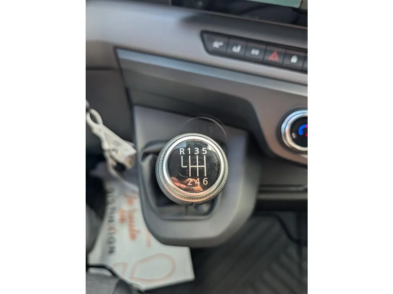 Gros plan sur le levier de vitesses manuel noir du Renault Master blanc, avec tableau de bord et commande de climatisation visibles.