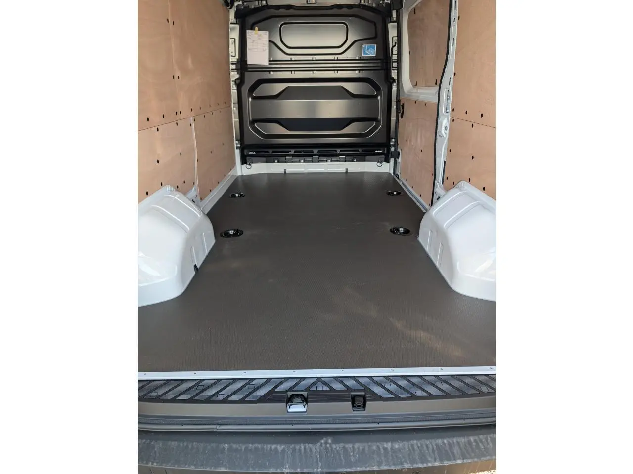 Intérieur du Renault Master 2025 vu de l'arrière, avec habillage bois latéral et plancher noir antidérapant.