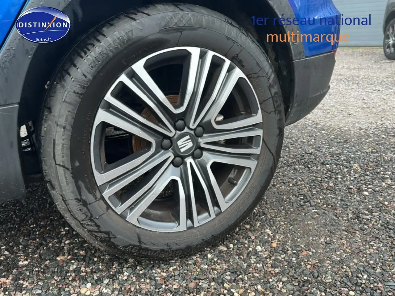 Gros plan sur la jante avant droite en alliage gris et noir du SEAT Arona bleu saphir, avec logo central Seat visible.