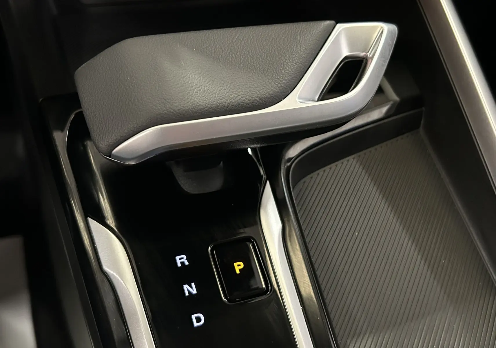 Gros plan sur la commande de boîte automatique noire et argentée du MG ZS hybride, avec le mode parking éclairé en jaune.