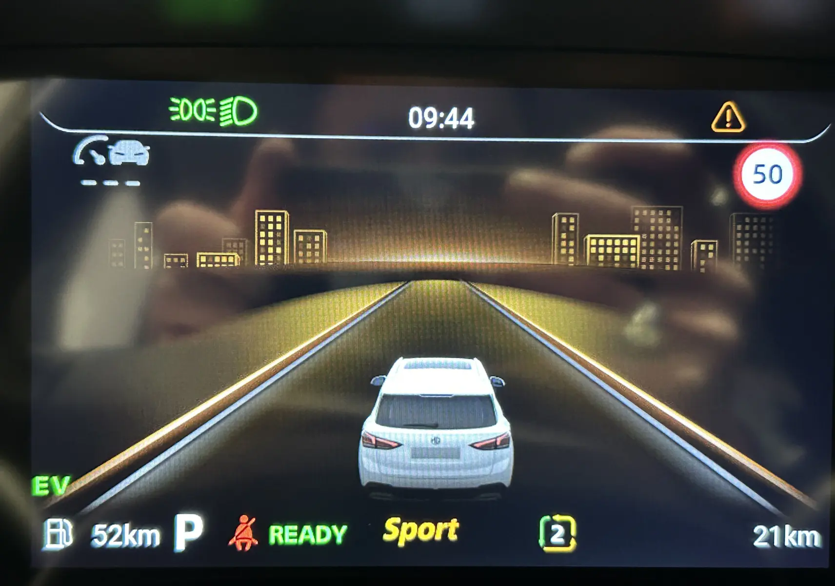 Affichage numérique montrant la MG ZS Cosmic Silver vue de l’arrière sur route virtuelle avec indication mode Sport et limite 50 km/h.
