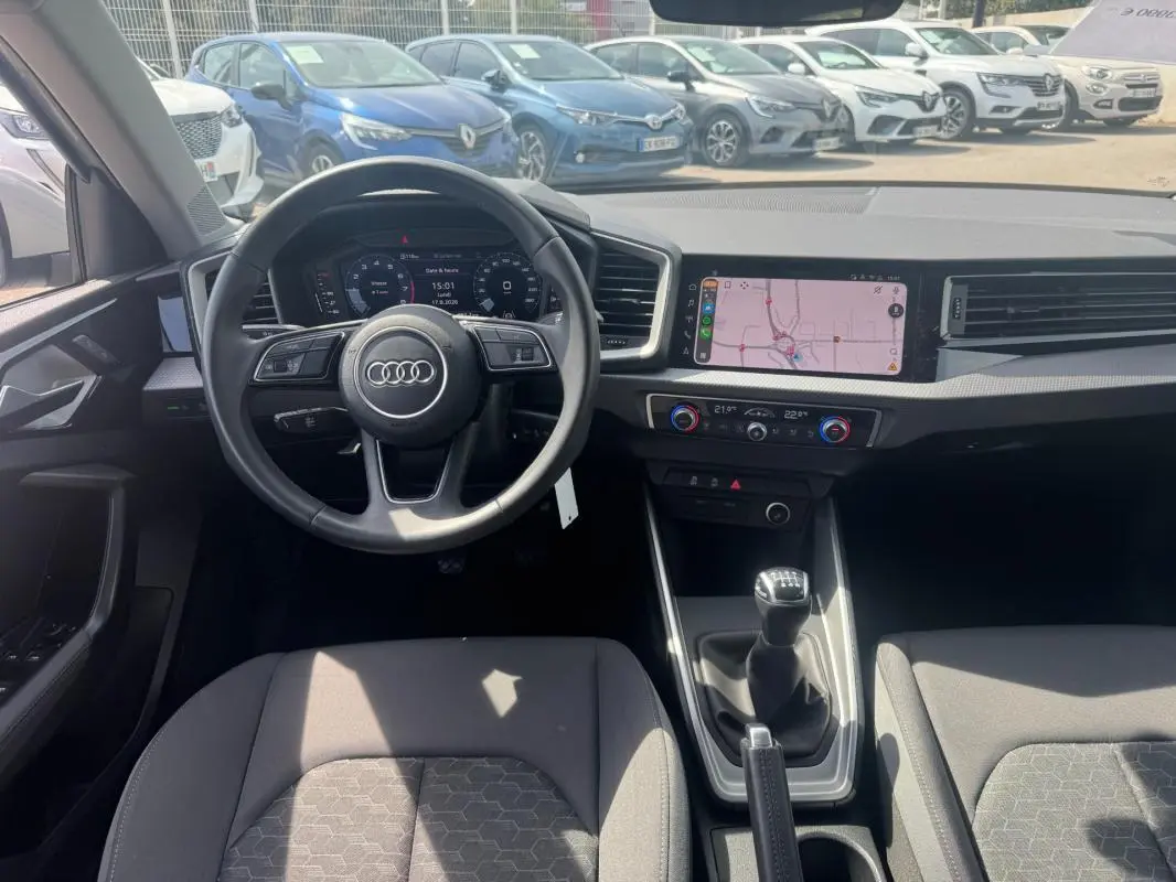 Vue intérieure avant de l'Audi A1 Sportback 2025 gris, volant cuir, cockpit numérique et boîte manuelle visible.