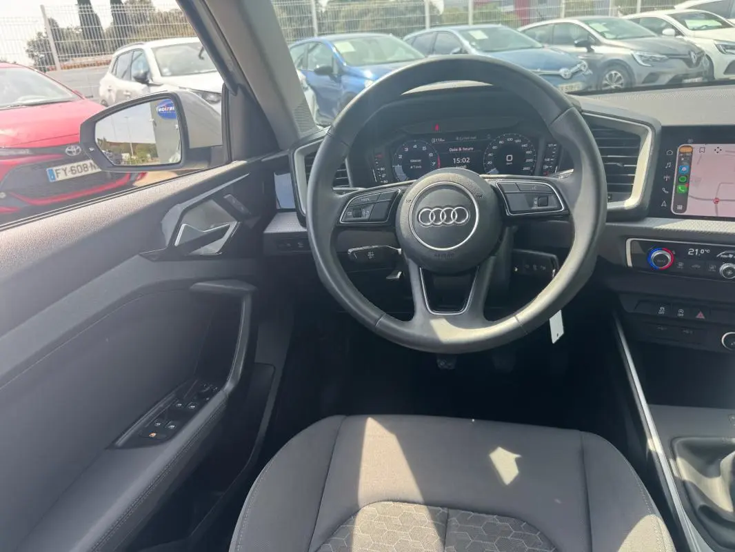 Vue intérieure avant de l'Audi A1 Sportback 2025 gris, volant cuir, cockpit numérique et écran tactile central visibles.