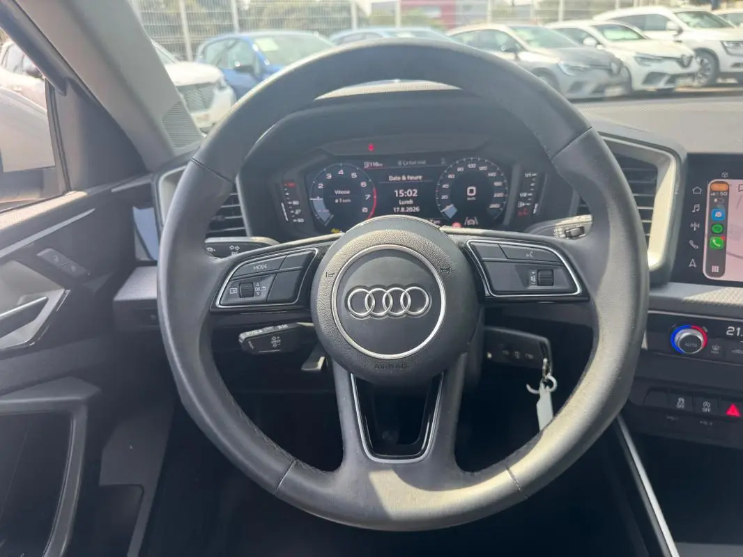 Vue intérieure centrée sur le volant cuir noir d'une Audi A1 Sportback 2025 avec cockpit numérique et commandes au volant.
