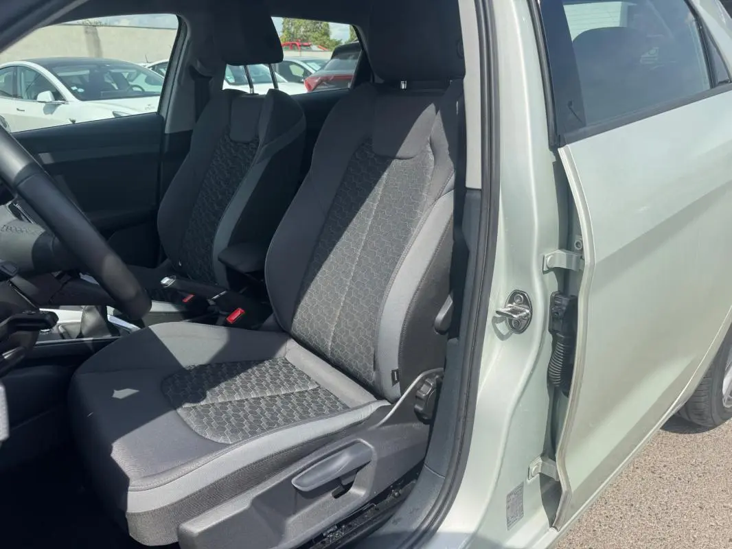 Vue intérieure côté conducteur de l'Audi A1 Sportback gris 2025, mettant en valeur les sièges sport en tissu et accoudoir central.