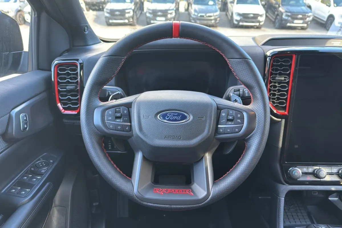 Vue intérieure centrée sur le volant noir du Ford Ranger Raptor 2024 avec surpiqûres rouges et aérateurs rouges.