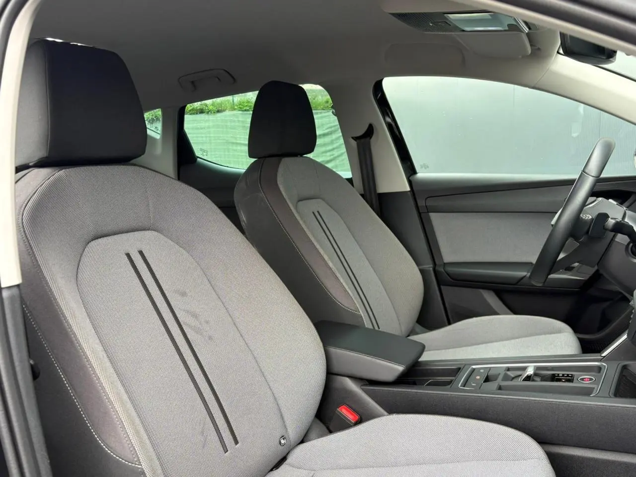 Vue intérieure côté droit montrant les sièges avant gris clair avec accoudoir central et volant cuir multifonction.