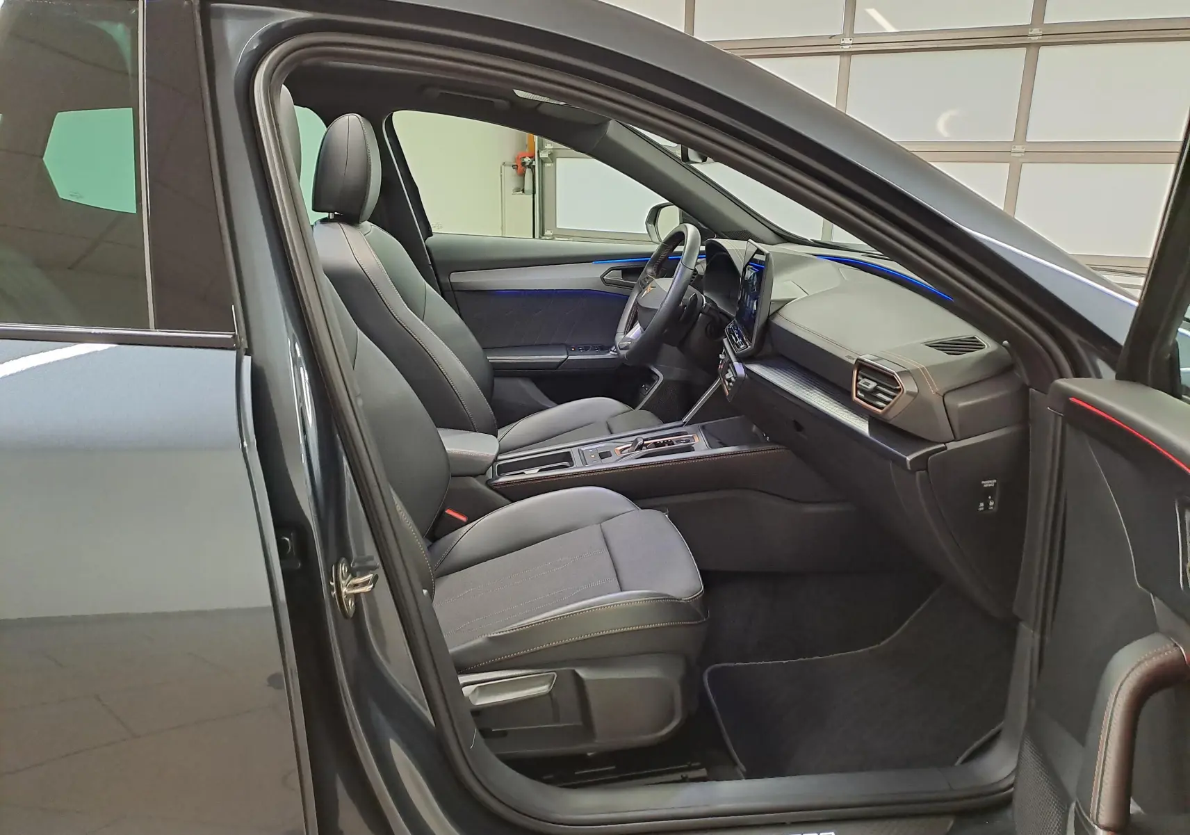 Vue intérieure côté conducteur de la CUPRA Formentor gris magnétique, avec sellerie noire et éclairage d'ambiance bleu.