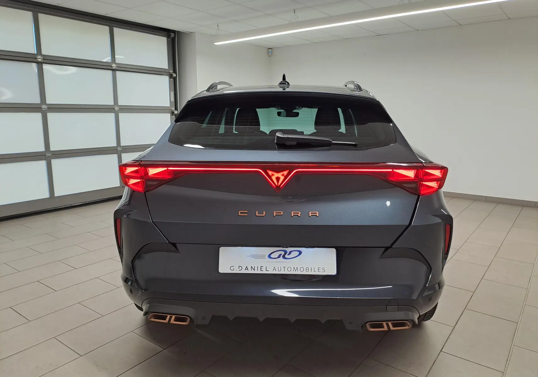 Vue arrière d'une CUPRA Formentor gris magnétique avec bandeau lumineux rouge et double sortie d'échappement cuivrée.