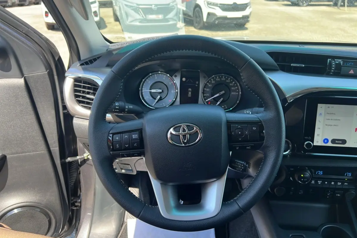 Vue intérieure centrée sur le volant cuir multifonctions du Toyota Hilux 2026, avec tableau de bord et écran tactile visible.