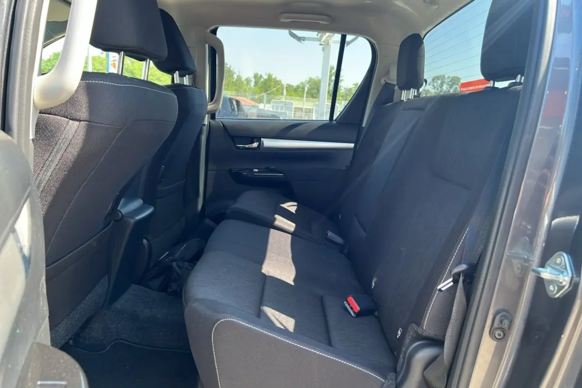 Vue intérieure arrière montrant la banquette tissu noire du Toyota Hilux 4x4 gris atlas avec porte ouverte côté droit.