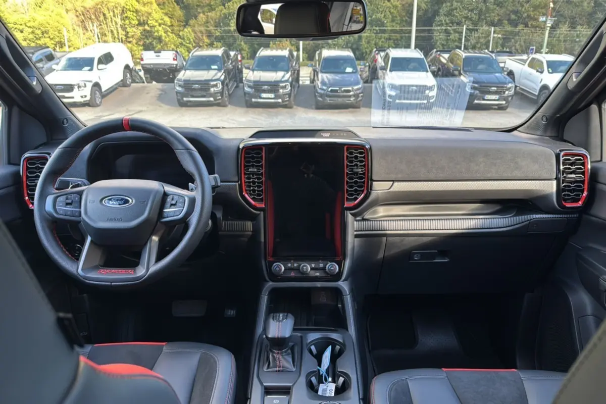 Vue intérieure avant du Ford Ranger Raptor 2024 noir absolu, avec volant sport et console centrale tactile verticale.